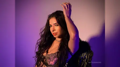 Young woman with long wavy hair in black lace lingerie posing against a purple studio background.