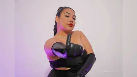 Confident woman in a black strapless outfit and gloves posing against a soft purple studio background.
