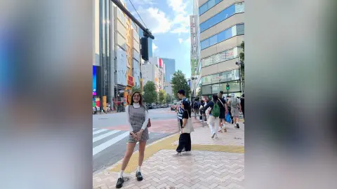 Stylish woman in a white sleeveless top and mini skirt walking on a sunny city street near modern buildings.