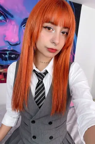 Samlion20 wears a grey waistcoat and striped tie with her long orange hair and blunt bangs, posing in front of a colorful face painting.