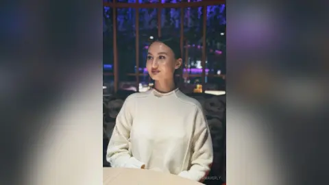 Smiling woman in a cozy white sweater sitting in a dimly lit restaurant with a moody atmosphere.