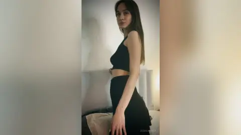 Young woman in a black crop top and skirt posing in a minimalist indoor setting with a moody aesthetic.