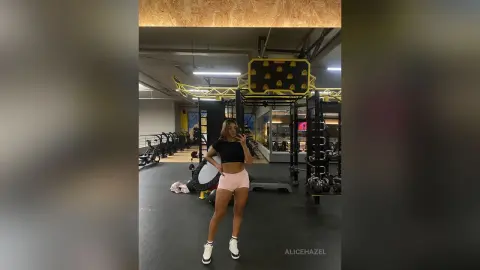 Fit woman in black crop top and pink shorts taking a mirror selfie in a modern gym setting.