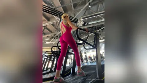 Athletic woman in pink yoga jumpsuit exercising on gym equipment in a bright modern fitness studio.