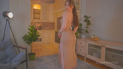 Elegant woman in a beige backless slit dress posing in a cozy, warm-lit modern kitchen setting.