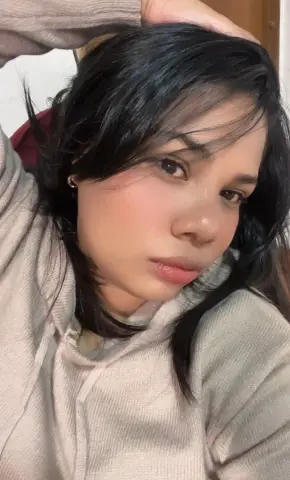 Young woman with dark hair wearing a cozy beige ribbed sweater in a relaxed indoor setting.
