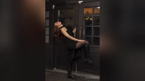 Elegant woman in a black dress and boots posing confidently in front of dark vintage doors.