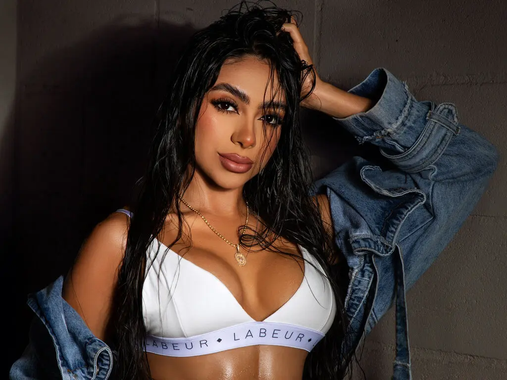 Young woman with wet hair in a white Labeur sports bra and denim jacket posing against a dark studio background.