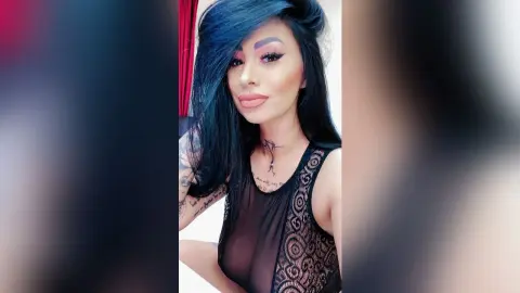 DeeaAnderson poses in a black lace tank top, showing her long blue hair and neck tattoo.