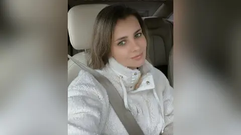 Smiling young woman in a cozy white fleece pullover sitting in a car seat.