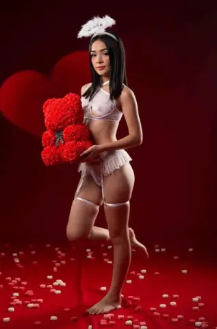 Young woman in white lace lingerie holding a red teddy bear against a romantic red heart background.
