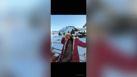 Smiling woman in a red puffer jacket and beanie enjoying a sunny winter day in the snowy mountains.