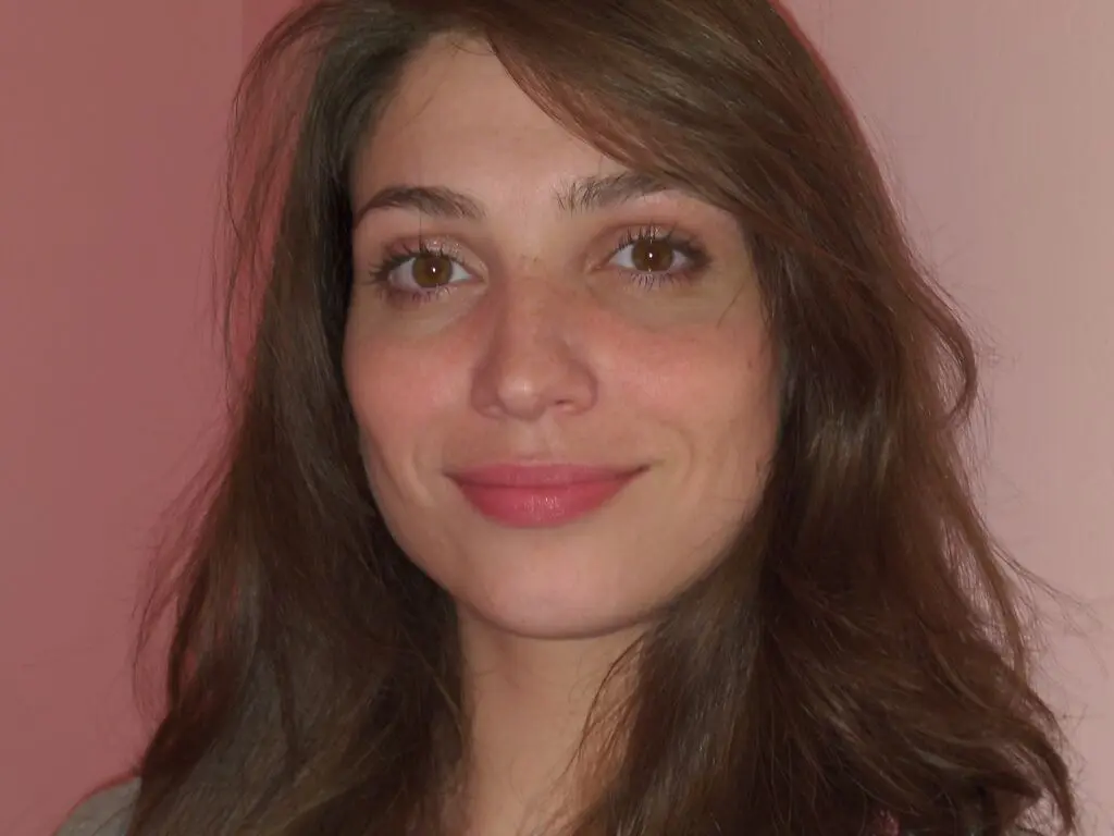 MarsieAbbadie smiling with long brown hair against a pink background.