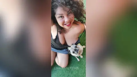 Smiling woman in a black polka dot sundress relaxing outdoors with her cute pug dog.
