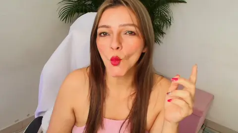 Smiling woman in a pink top making a playful kissy face in a bright indoor setting.