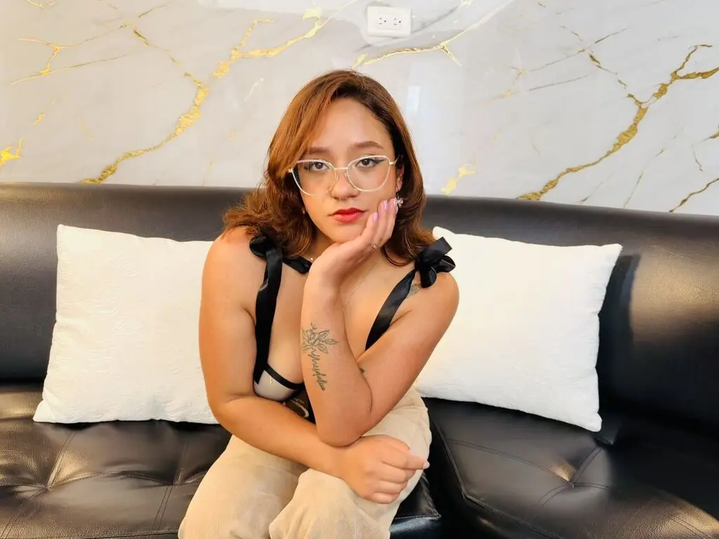Young woman in glasses and black camisole relaxing on a black leather sofa against a marble wall.