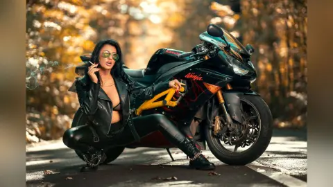 MissyJolie wears a black leather jacket and tight leggings while squatting next to a black Ninja motorcycle, holding a cigarette with smoke rising.