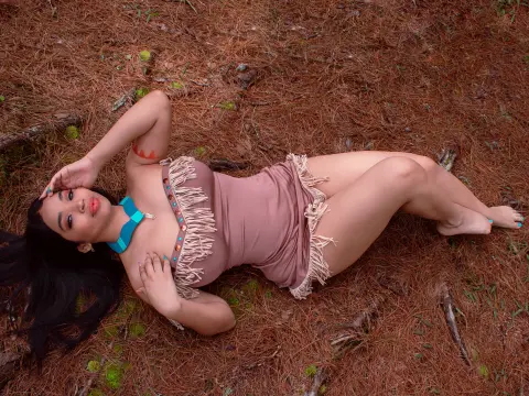 Woman in a dusty rose fringed bodysuit lying on a bed of pine needles in a peaceful forest setting.