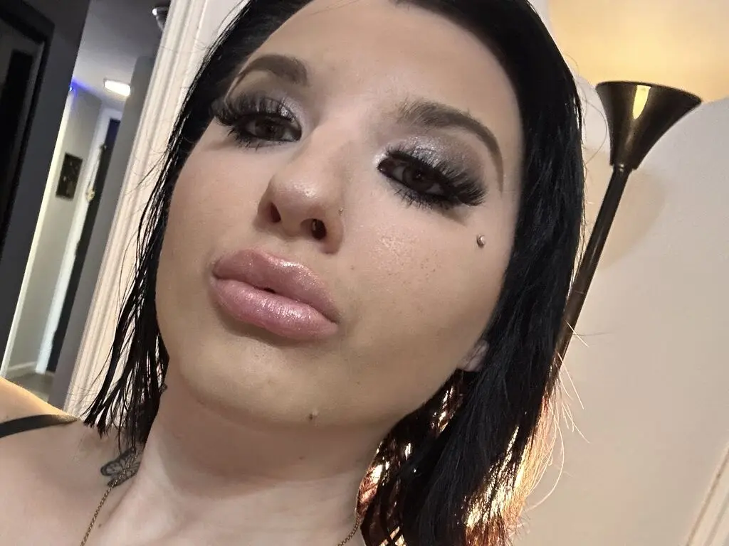 Close-up portrait of a woman with dark hair and dramatic smoky eye makeup in a warm indoor setting.