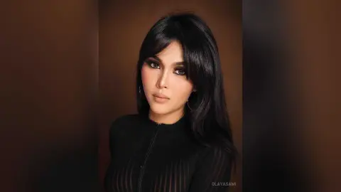 Elegant woman with long dark hair and glamorous makeup wearing a black ribbed turtleneck in a moody studio setting.
