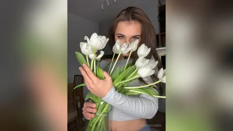 StasyScorpio — StasyScorpio holds a large bouquet of white tulips in front of her face while wearing a grey long-sleeve crop top.