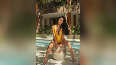 Beautiful woman in a yellow swimsuit sitting by a tropical resort swimming pool on a sunny day.