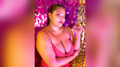 Confident woman in a red low-cut dress posing against a glamorous pink and gold shimmering background.