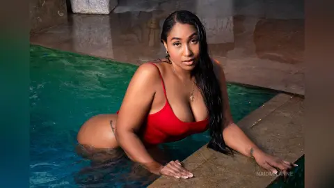 NaiomiLanne — Curvy woman in a red one-piece swimsuit relaxing in a luxury swimming pool on a sunny day.