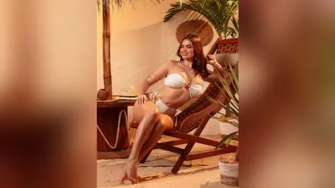 Smiling woman in a white bikini relaxing in a wooden lounge chair at a tropical beach resort setting.