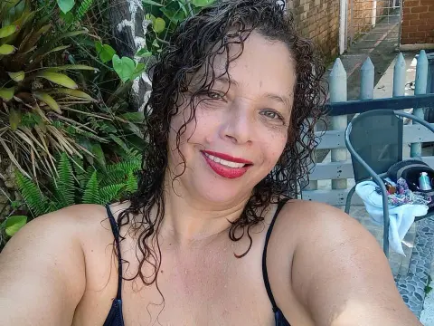 Smiling woman with curly hair in a black bikini relaxing in a lush tropical garden setting.