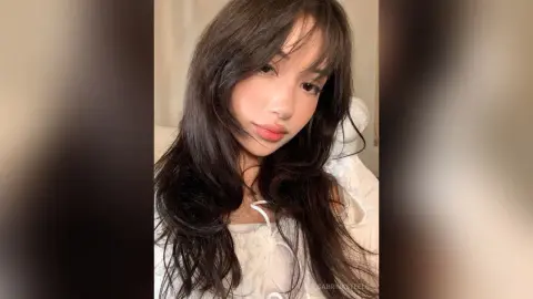 SabrinaSteels poses with long, dark wavy hair and a white off-the-shoulder top, looking directly at the camera.