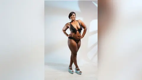Confident curvy Black woman in a black lace bikini posing in a bright studio setting.