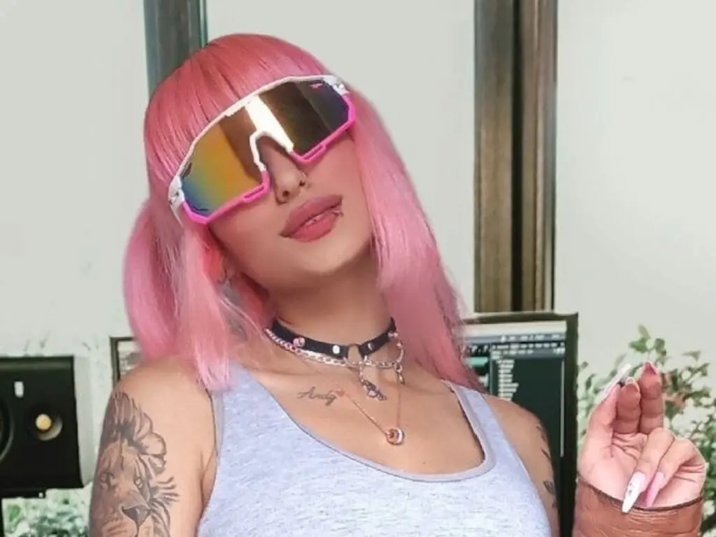 BarbieSimpsom wears pink hair and reflective sunglasses, posing in a grey tank top and black choker with a silver chain necklace.