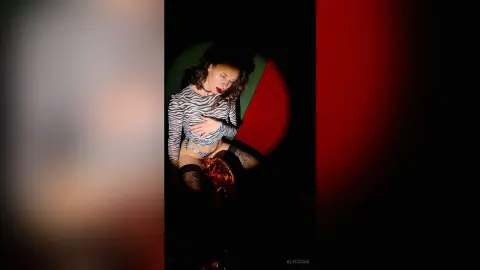 Woman in striped long-sleeve top and patterned tights posing in moody, dramatic red and black lighting.