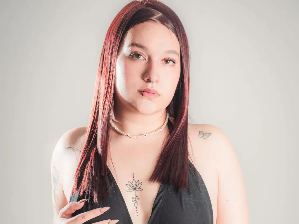 Young woman with long red hair and nose piercing wearing a black halter top against a plain white background.
