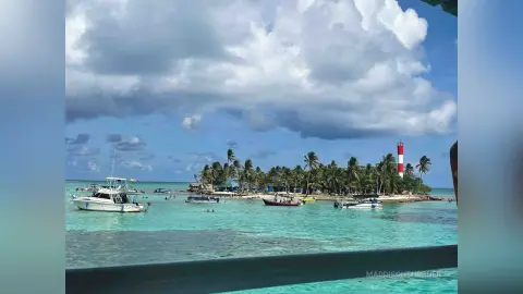 Tropical turquoise ocean view with white boats floating near a lush island under a cloudy sky.