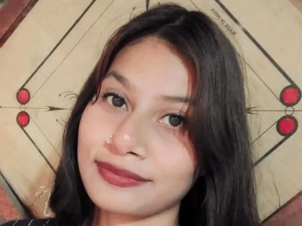 Young woman with long dark hair smiling in a casual indoor setting.