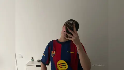 Young woman in a blue and red FC Barcelona jersey taking a mirror selfie in a bright minimalist room.