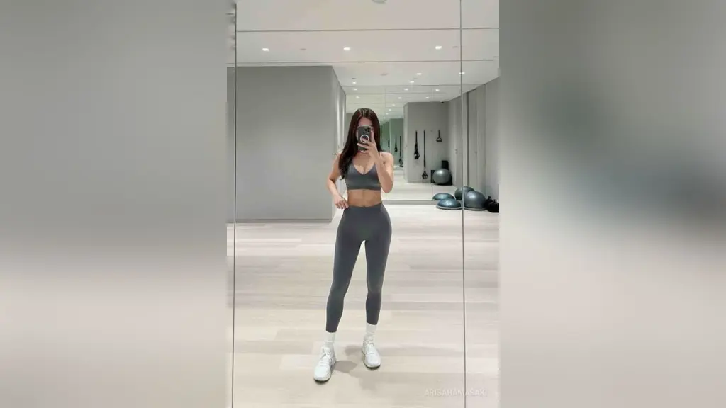 ArisaHamasaki — Fit woman in grey yoga set taking a mirror selfie in a bright, modern minimalist home gym studio.