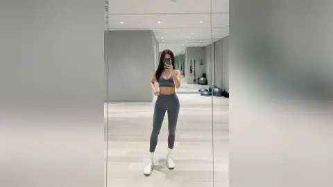 ArisaHamasaki — Fit woman in grey yoga set taking a mirror selfie in a bright, modern minimalist home gym studio.