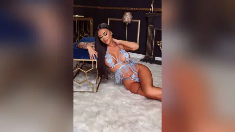 Glamorous woman in a light blue feathered bodysuit lounging on a white shag rug in a luxury dark interior.