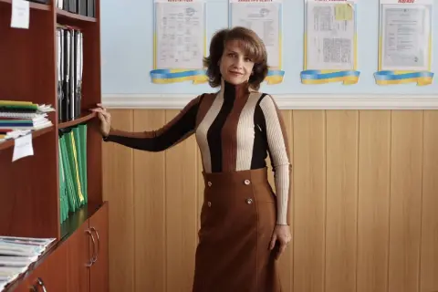 Smiling professional woman in a brown turtleneck and skirt standing in a modern office setting.