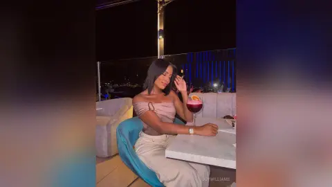 Stylish woman in a beige off-the-shoulder top enjoying a cocktail at a rooftop lounge at night.