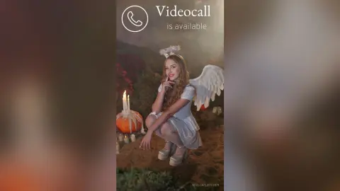 StellaFletcher wears white angel wings and a white lace dress while sitting outdoors near a lit pumpkin and candle.