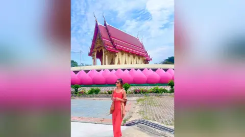 Woman in a red summer outfit standing before a traditional pink Thai temple under a bright blue sky.