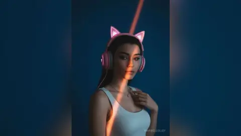 Young woman wearing glowing pink cat ear headphones in moody blue lighting.