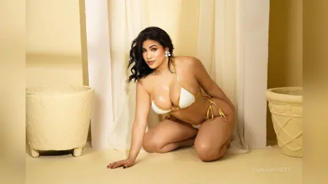 Beautiful woman in a white bikini posing gracefully in a bright, minimalist studio setting.