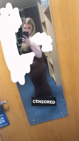 Blonde woman in a brown bodycon dress taking a mirror selfie in a casual indoor setting.