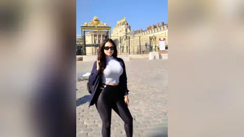 Stylish woman in black leggings and white top posing in front of a grand Parisian palace on a sunny day.