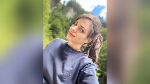 Smiling young woman in a navy blue sweatshirt relaxing in a lush green forest setting.